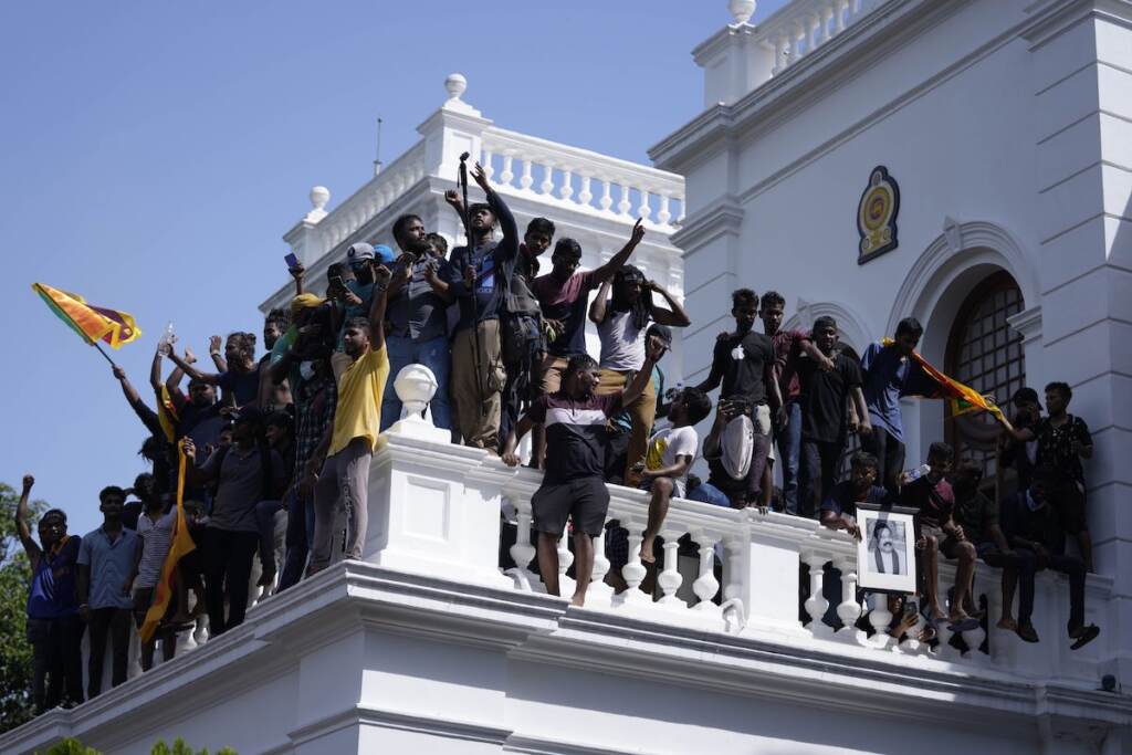 Sri Lankan protesters, some holding national flags, after storming the Prime Minister Ranil Wickremesinghe's office, demanding he resign after president Gotabaya Rajapaksa fled the country amid economic crisis in Colombo, Sri Lanka, Wednesday, July 13, 2022. (AP Photo/Eranga Jayawardena)