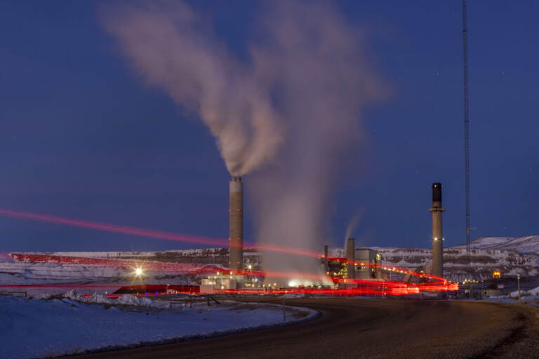 Smoke rises from a power plant, as the lights glow red in a snowy landscape at night.