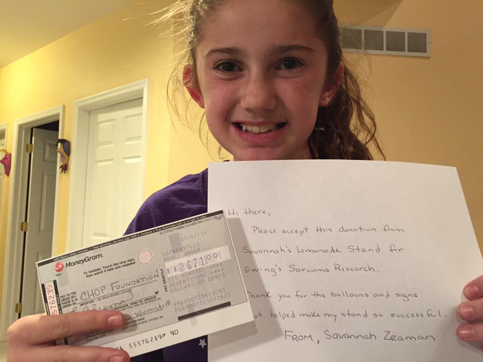 Savannah holding a check and message for CHOP cancer reasearch