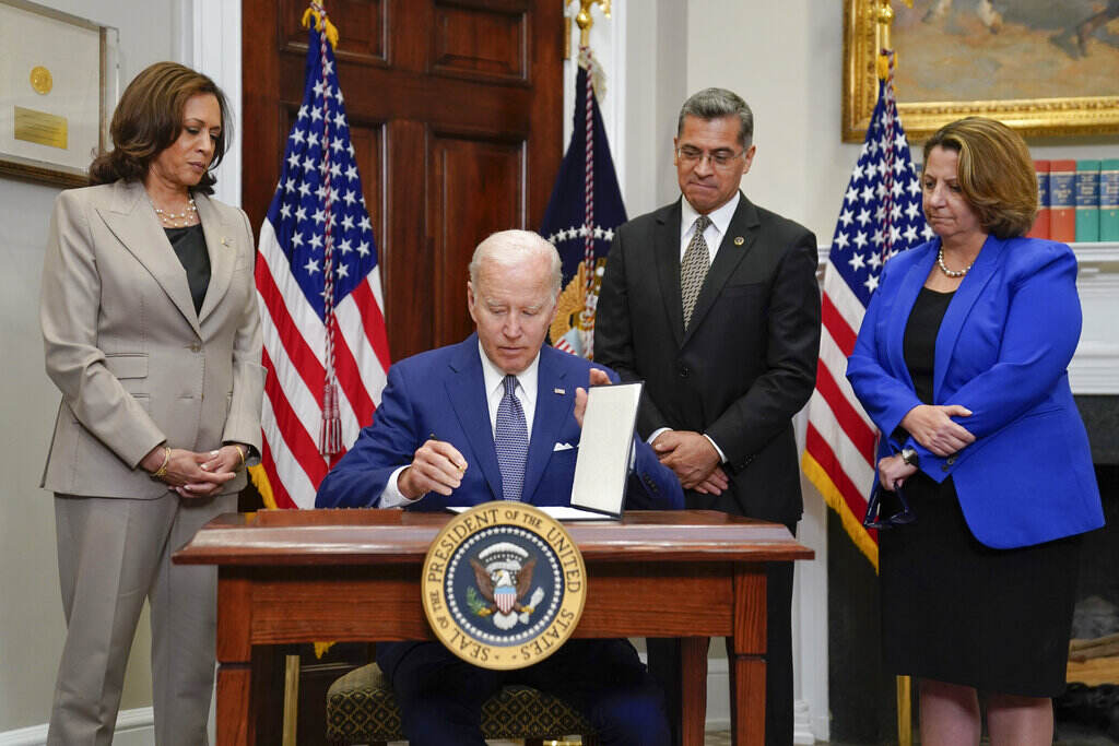 Biden Abortion President Biden sits at a desk, signing an order, as Vice President Kamala Harris and others stand and look on.