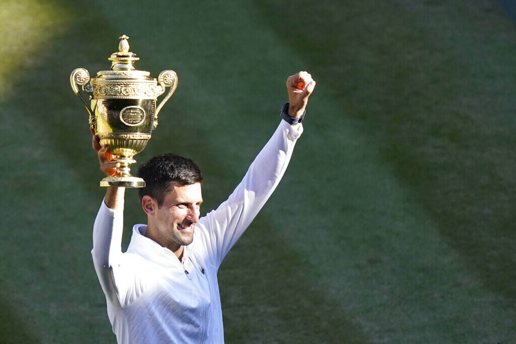 Britain Wimbledon Tennis Djokovic holds the Wimbledon trophy up in the air with one hand as he raises his arms.