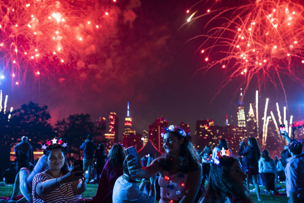 July Fourth New York People smile as fireworks go off overhead.