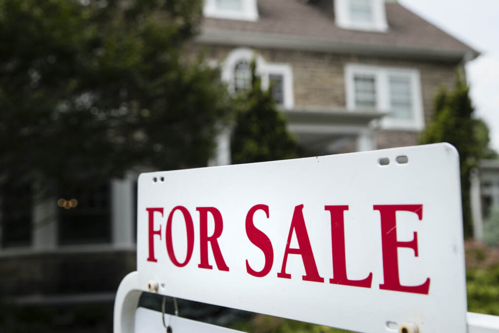 A 'for sale' sign stands in front of a house