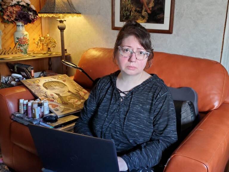 A woman sits in an armchair with a laptop in front of her.