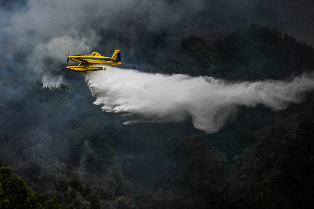 A firefighter aircraft drops water in a wildfire in Portugal on Saturday. A helicopter sprays water, as forests are visible below.