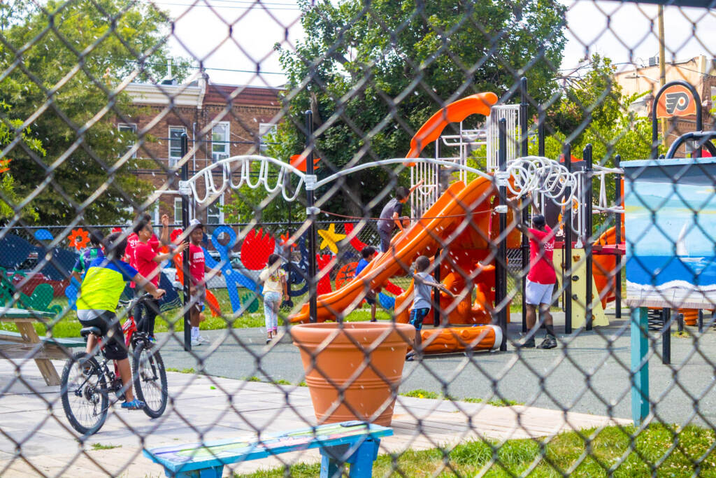 Kids play on a playground as seen through a fence in the foreground.