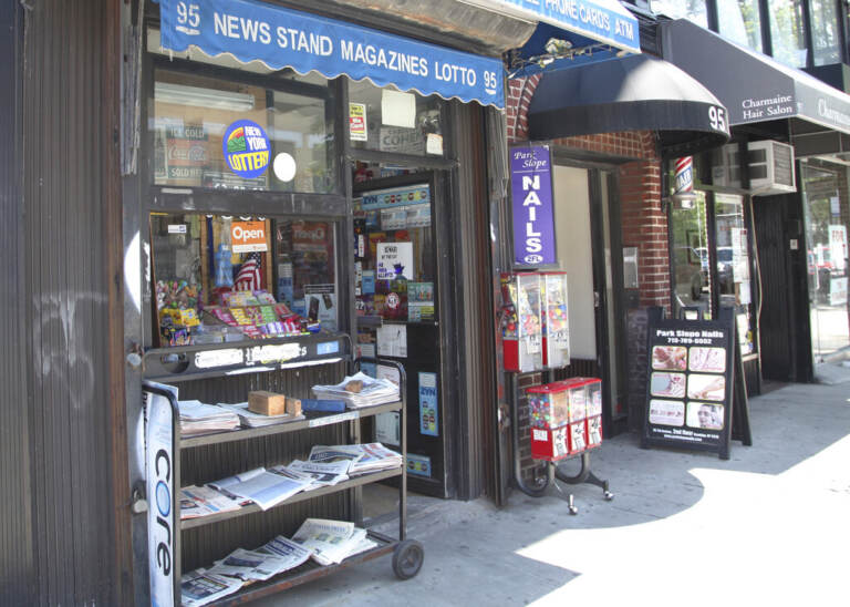 A newspaper stand is visible on a sunny day.