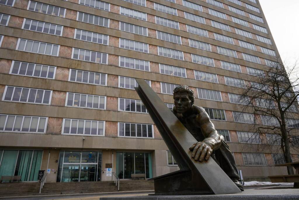 A statue of someone holding up something is visible in front of a tall building.