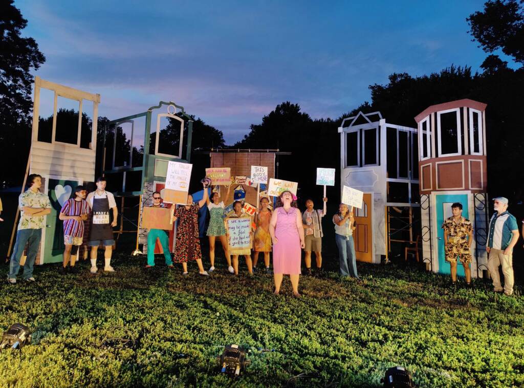 shakespeare-clark-park-p-crimmins-2022-07-27-3 Minou Pourshariati as Bianca leads the Actively Conscious Chorus through a protest song in 'The Tamer Tamed,' opening the second act of Shakespeare in Clark Park’s production of 'The Taming!' set in West Philly circa 1990s. (Peter Crimmins / WHYY)