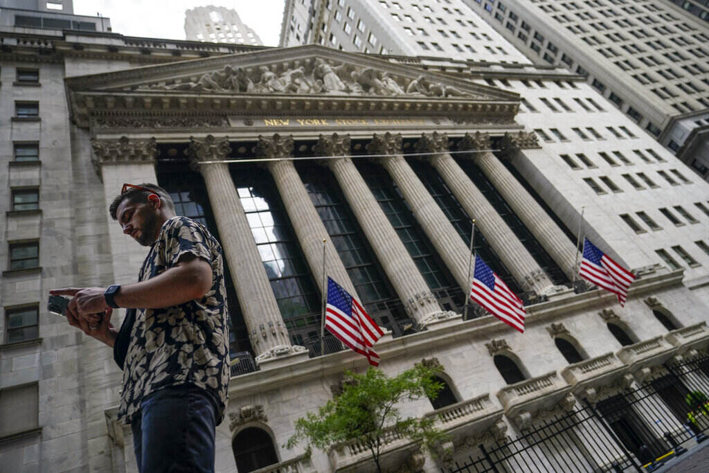A man stares down at his cellphone as the stock exchange building in New York is visible in the background.