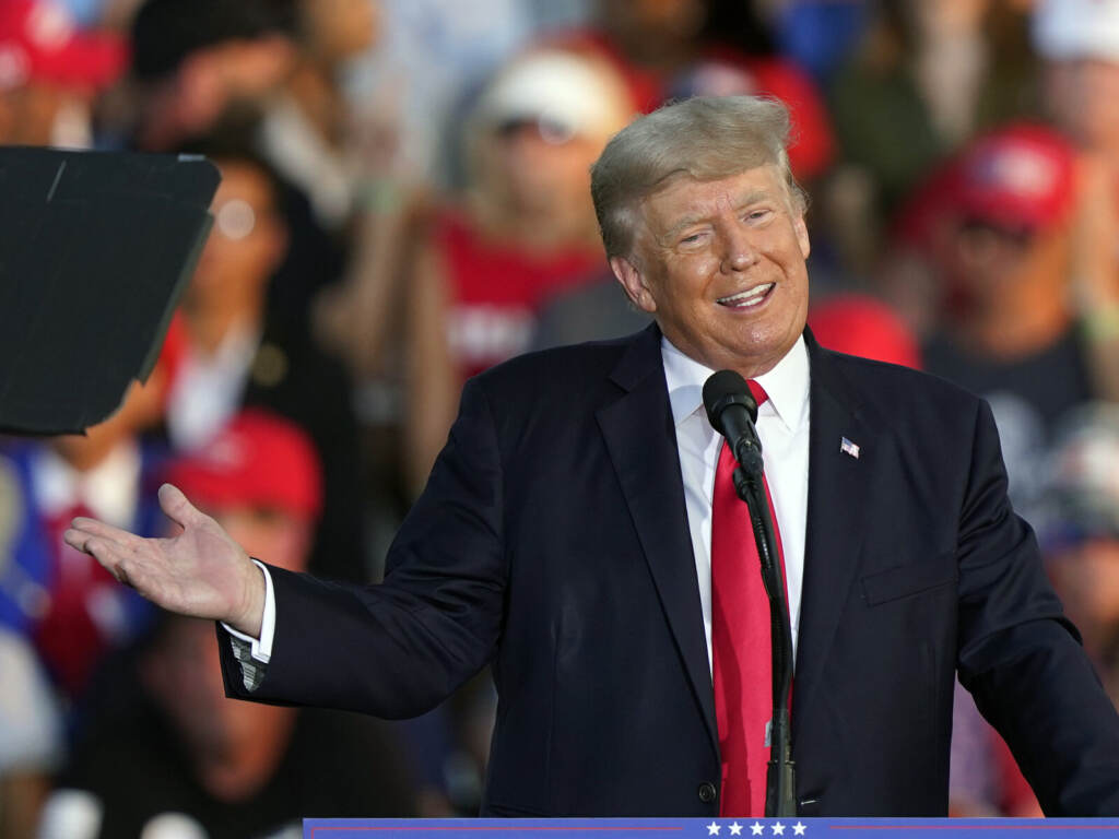 Donald Trump Former President Donald Trump speaks at a microphone while gesturing with his hands.