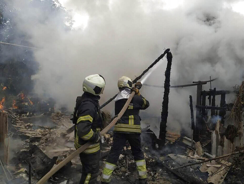 Russia Ukraine War Firemen hold a hose, pointing water toward a cloud of smoke.