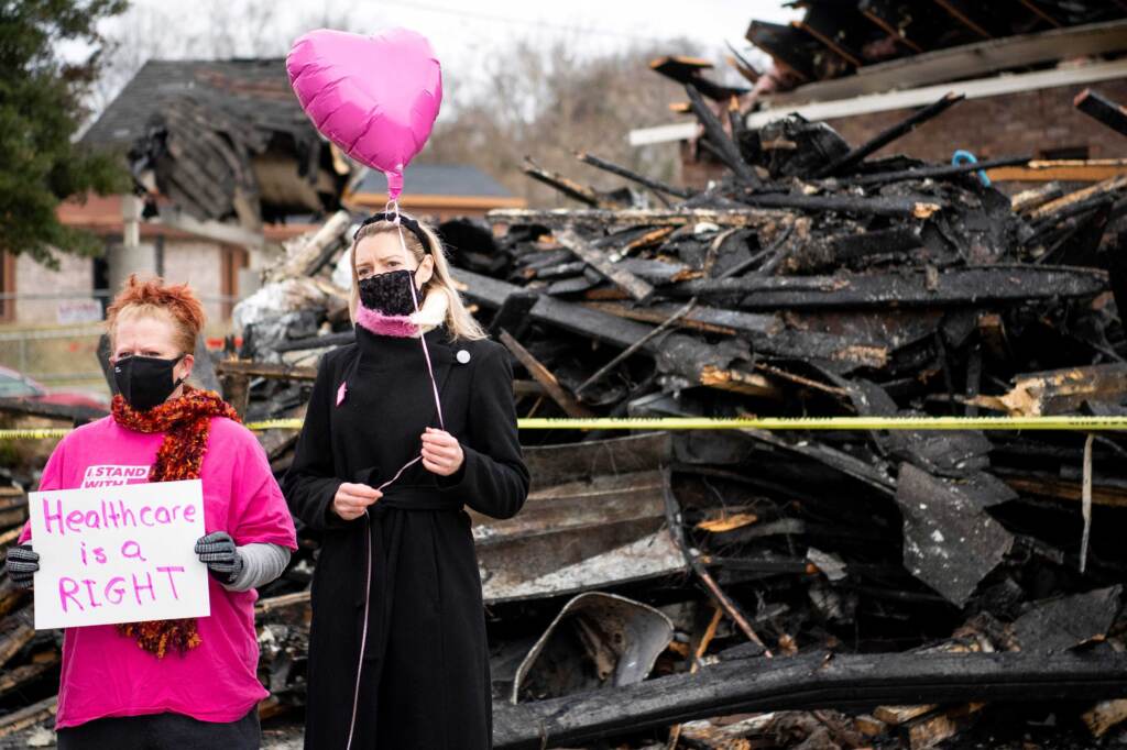 Supporters stand in front of a pile of fire burned wreckage at Knoxville’s Planned Parenthood on Jan. 6. Two people holds a pink balloon in front of a pile of burnt wreckage.