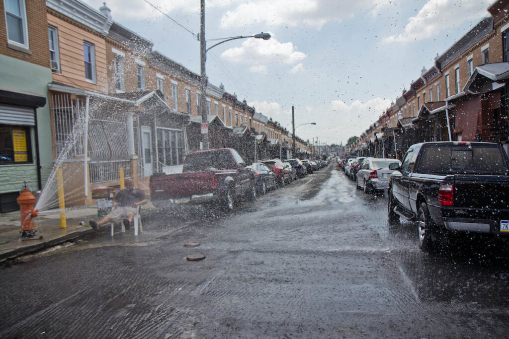 man sits on a chair in the path of a fire hydrant's spray