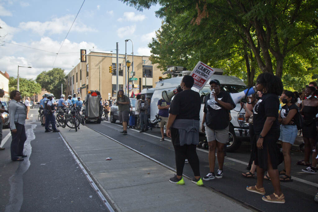 2022 08 08 k paynter general UC townhomes encampment eviction attempt (1 of 1) A crowd gathers on a sidewalk in front of an apartment building.