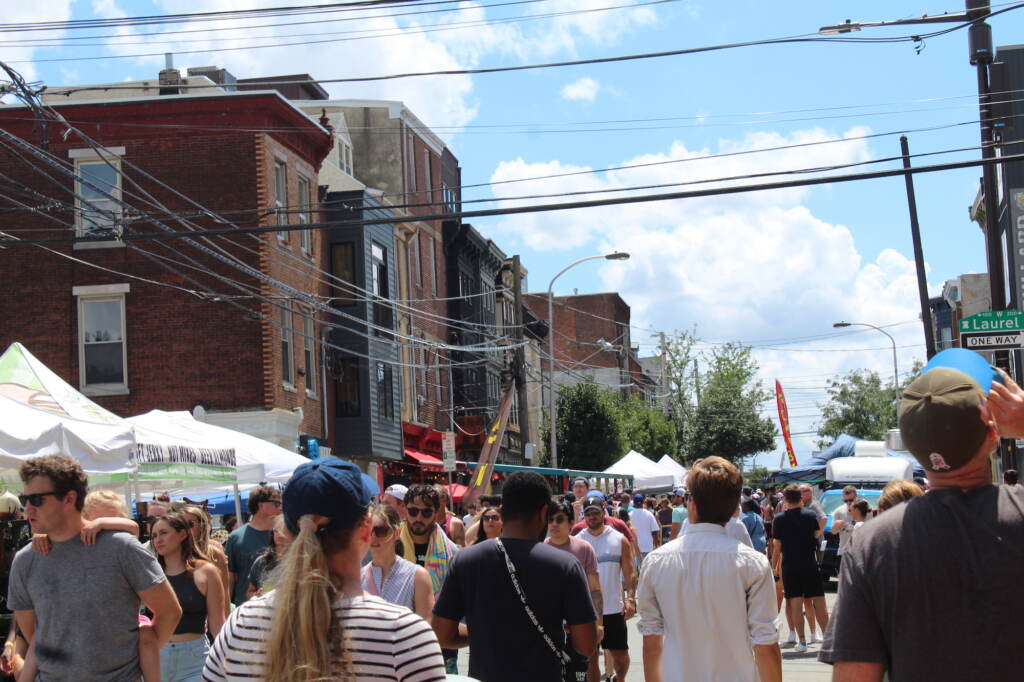 2nd-street-festival-crowd-08-07-22 A crowd walks down a street. Buildings are visible in the background.