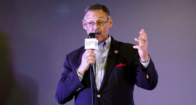 A man gestures while holding a microphone.