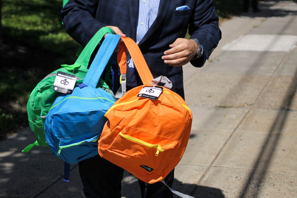 backpacks-giveaway-081022 A person holds up three colorful backpacks.