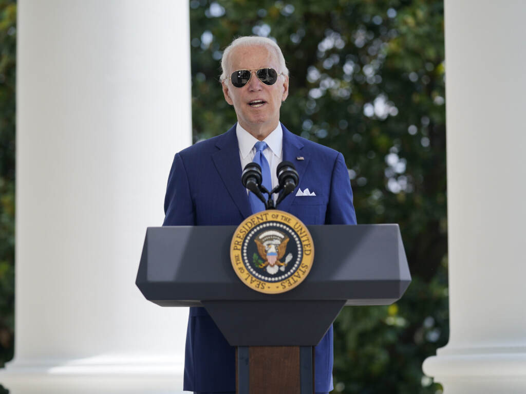 Joe Biden President Biden speaks at a podium wearing sunglasses.