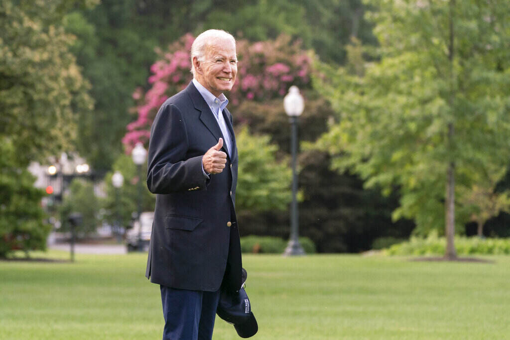 Joe Biden President Biden smiles and gives a thumbs up sign. Trees and grass are visible in the background.