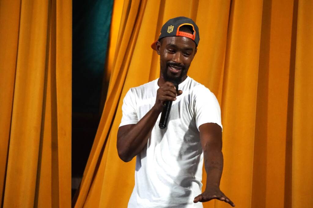 drill-music-philly-anti-violence-1 A person holds a microphone and gestures. Stage curtains are visible in the background.
