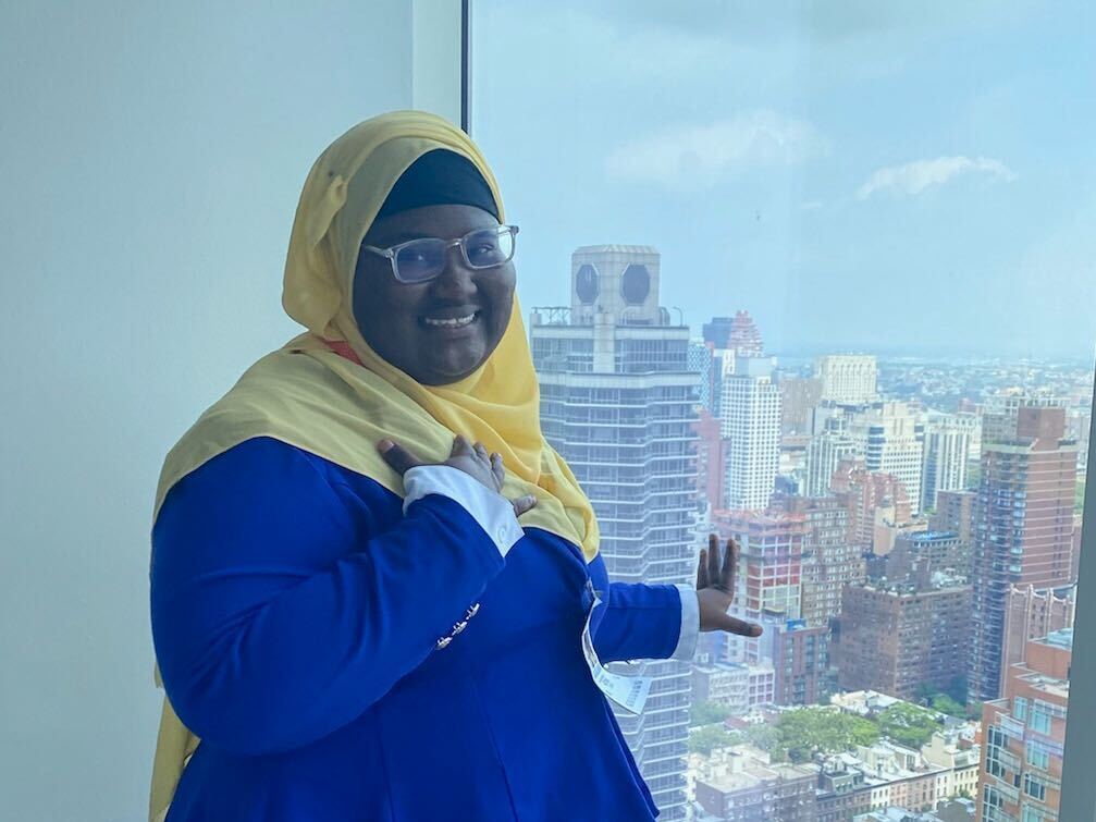 Fatimata Cham stands in front of a glass window inside the Bloomberg office