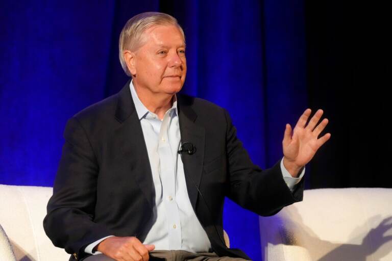 Sen. Lindsey Graham sits in a chair and appears to wave to an audience.