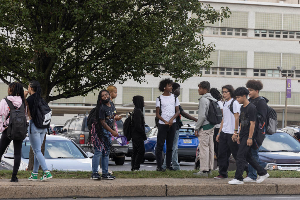 Groups of students laugh and talk outside of their school building.