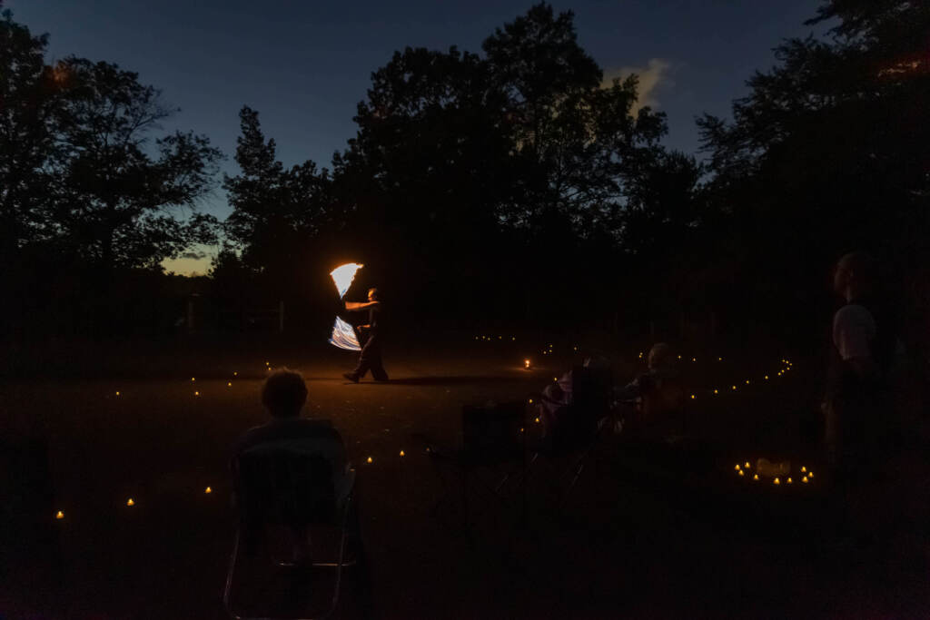 09 22 2022 k paynter fire spinning equinox celebration runnemade labyrinth A person performs fire spinning in a darkened field as people look on.