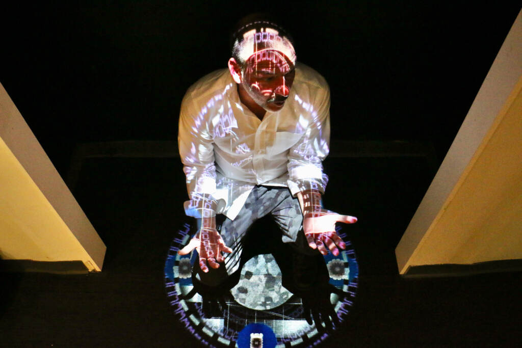 2022 09 08-e lee-joseph lazaro rodriguez-philadelphia national liberty museum-truth exhibit light Joseph Lazaro Rodriguez crouches beneath his digital projection, ''Chromatherapeutics: Veritas DS,'' on display at the National Liberty Museum. Rodriquez's works complement the museum's exhibit about truth. (Emma Lee/WHYY)