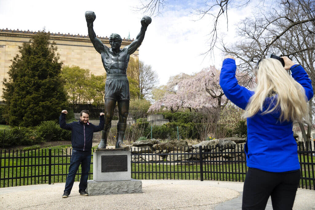 T25 Sports Movies Rocky File: In this April 3, 2020, photo, Jessica Shiroff (right) directs exchange student Joao Martucci, of Brazil, as he poses for a photo with the Rocky Statue at the Philadelphia Art Museum in Philadelphia.