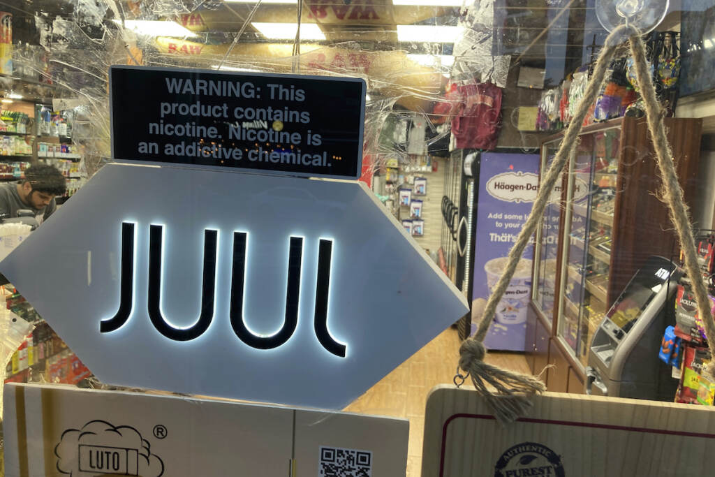 Juul Vaping Settlement File photo: A Juul electronic cigarette sign hangs in the front window of a bodega convenience store in New York City on June 25, 2022. (AP Photo/Ted Shaffrey, File)