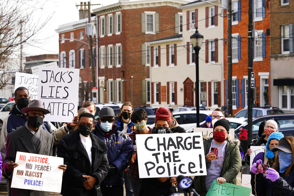 Shooting Outside Football Game People gather holding signs that read Charge the police. Rowhomes are visible in the background.