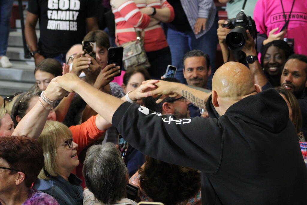 Fetterman is seen from behind, reaching out his hands to attendees of the rally.