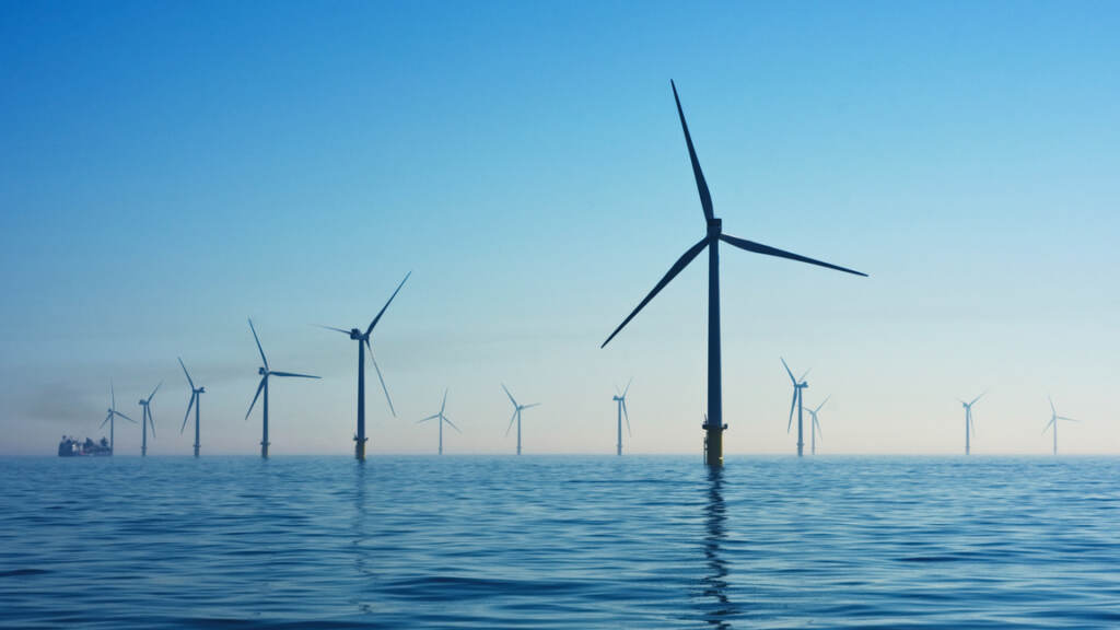 Offshore-wind-farm-clean-energy-power Offshore wind turbines are visible stretching into the distance with blue sky in the background.