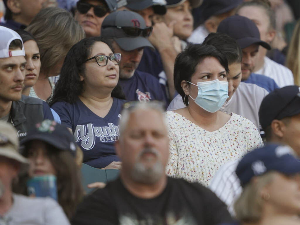 A person in the stands wears a mask before Dr. Anthony Fauci threw out the first pitch, at a baseball game between the Seattle Mariners and the New York Yankees, on Aug. 9 in Seattle. Fauci is President Biden’s chief medical adviser and director of the National Institute of Allergy and Infectious Diseases. A crowd of people are visible, most not wearing masks, one person wearing a blue surgical mask.