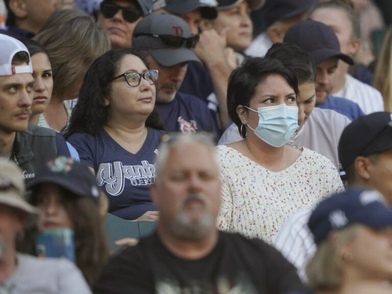 A crowd of people are visible, most not wearing masks, one person wearing a blue surgical mask.