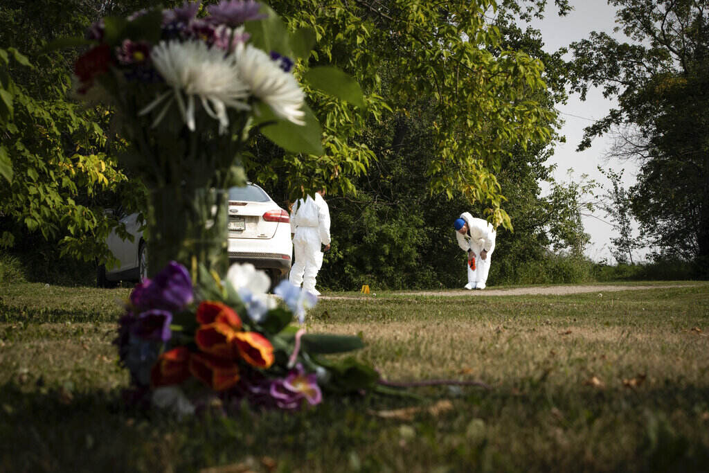 Canada Stabbings A close-up of flowers on the ground, with an investigator examining a crime scene in the background.