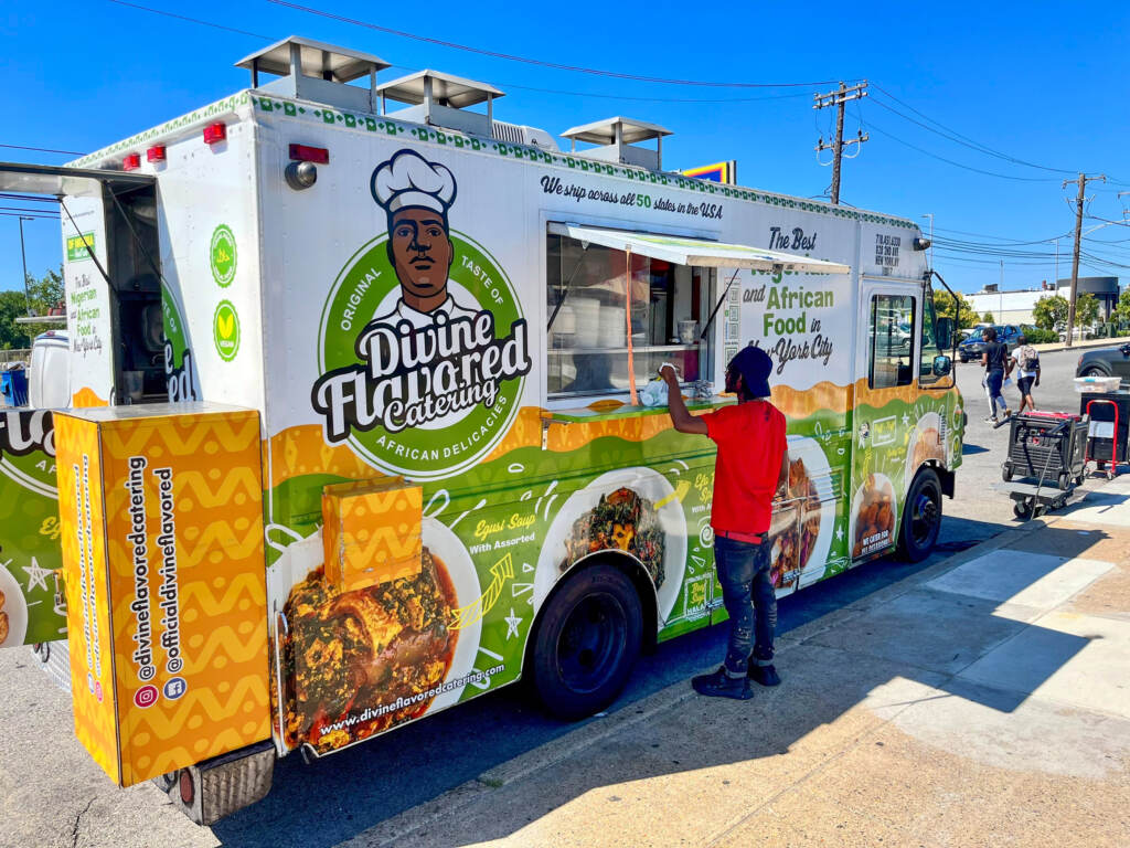 dfnigeria-foodtruck-01 A person in a red shirt orders from a brightly colored green and white food truck.