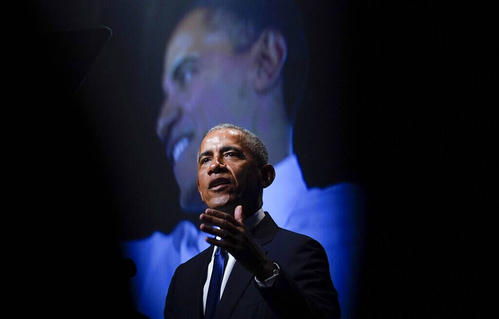 Barack Obama Obama speaks on stage, with an image of Obama showing in the background.
