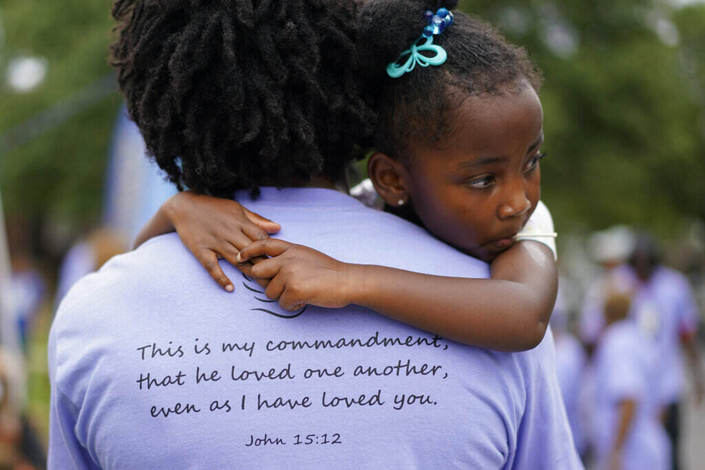 Blair McCloud A little girl looks over the shoulder of an adult wearing a shirt which has a Bible verse written on the back.