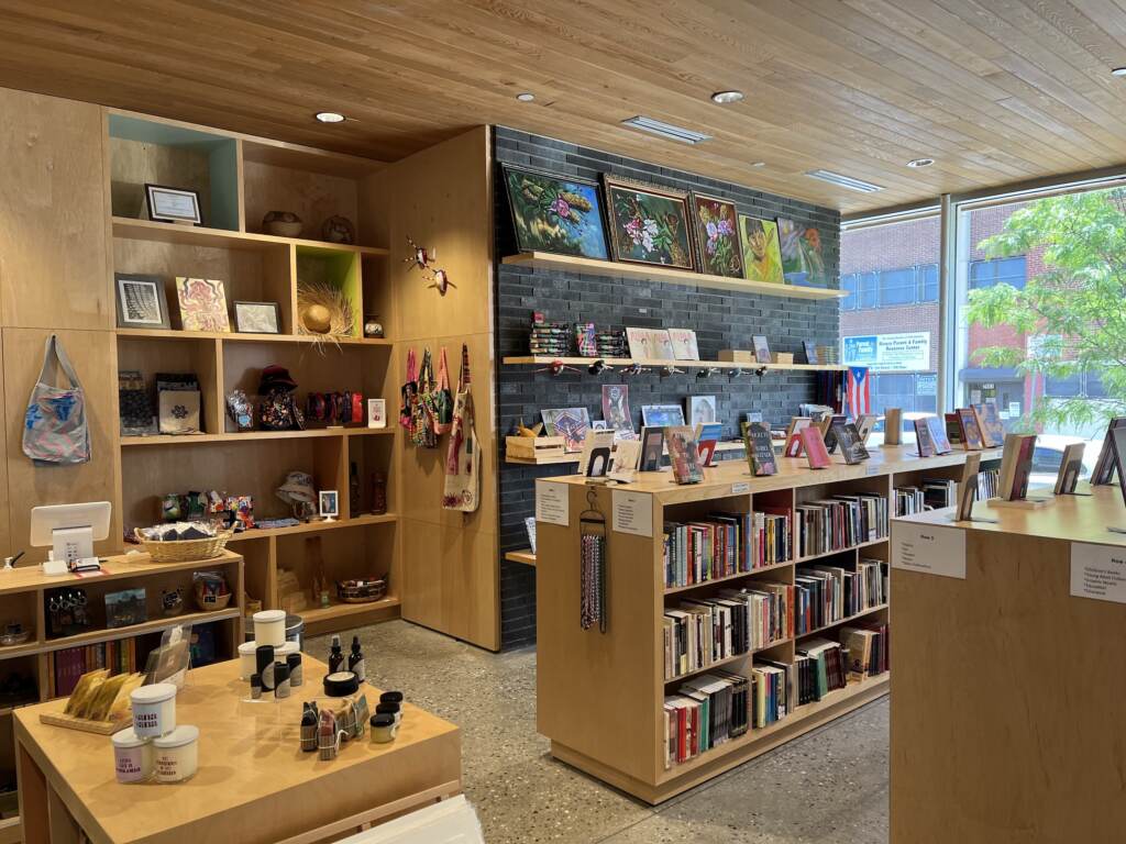 juliadeburgos-bookstore Shelves of books and artwork for sale is visible in a bookstore.