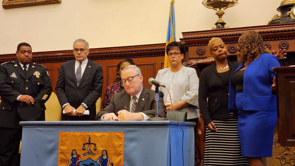 kenney-executive-order-gun-ban-parks-1 Mayor Kenney signs a document at a table surrounded by other elected officials.