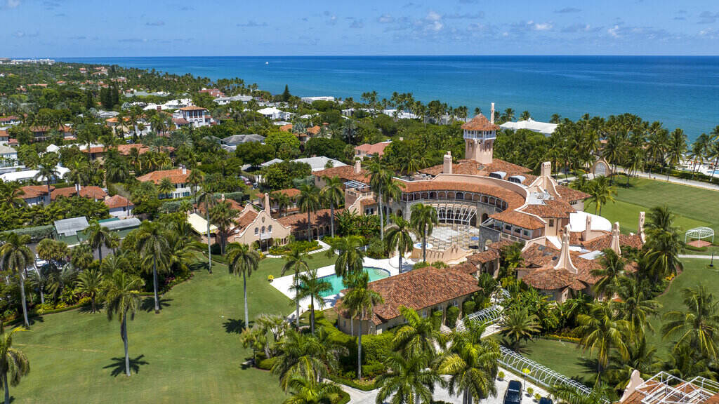 Trump FBI A view from above of a sprawling building with a pool and green laws, with a beach and ocean in the background.