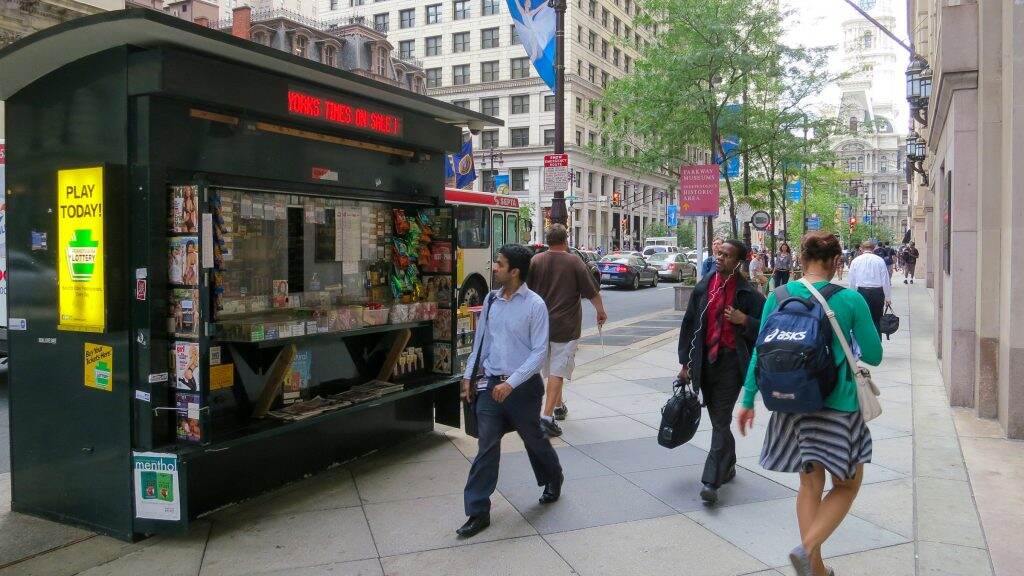 newsstand-centercity-1024×576 People walk by a newsstand on the sidewalk.