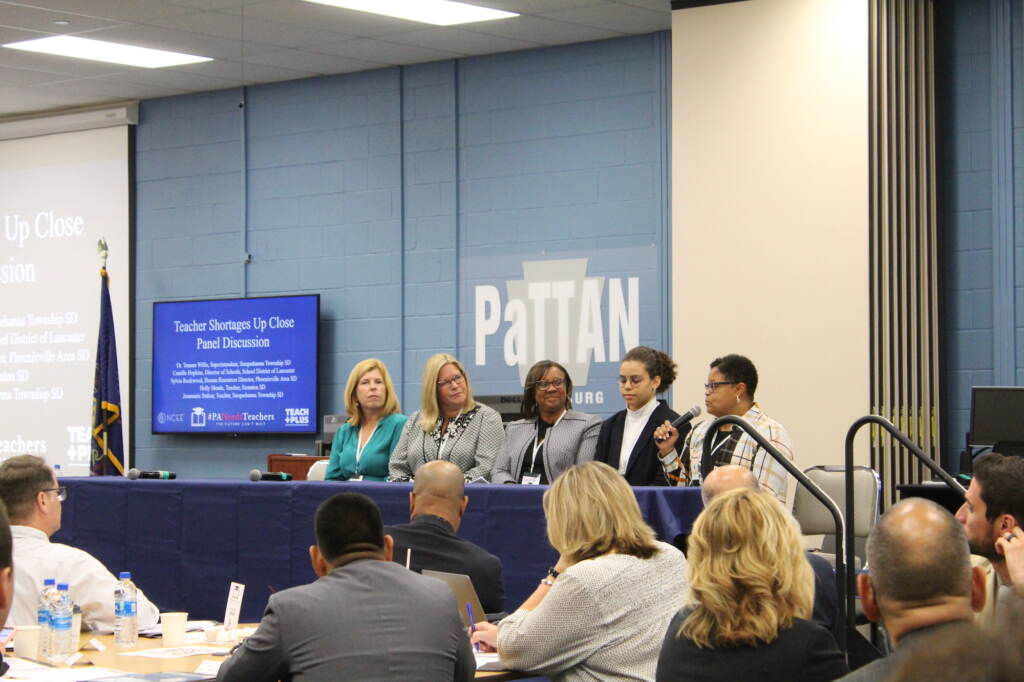 A group of people are seated at a table in front of an audience.