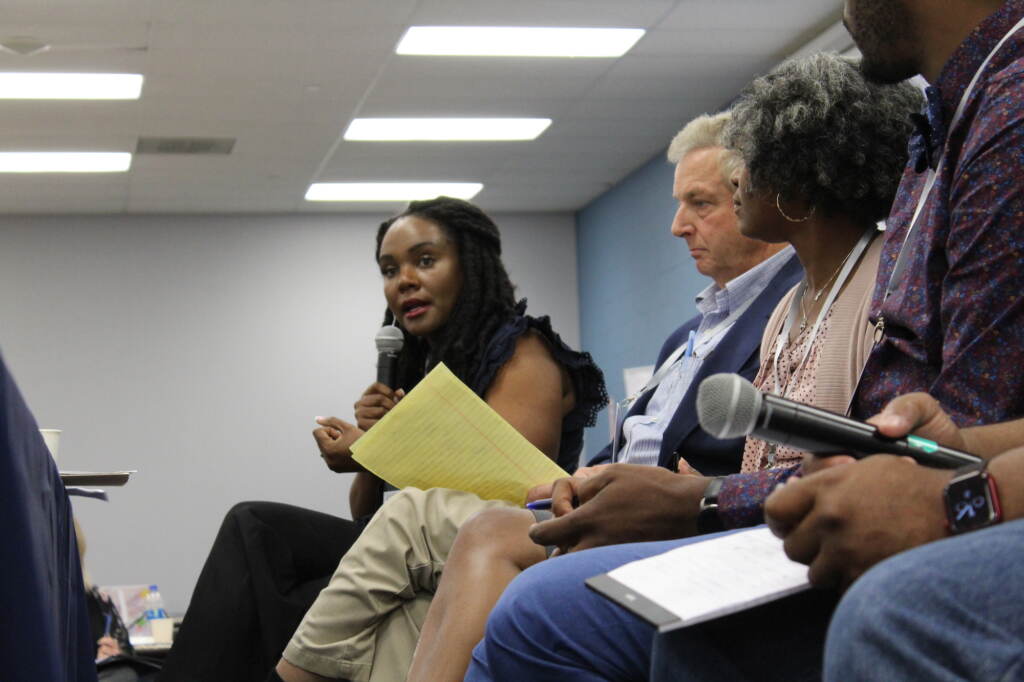 A woman speaks into a microphone as other people listen.