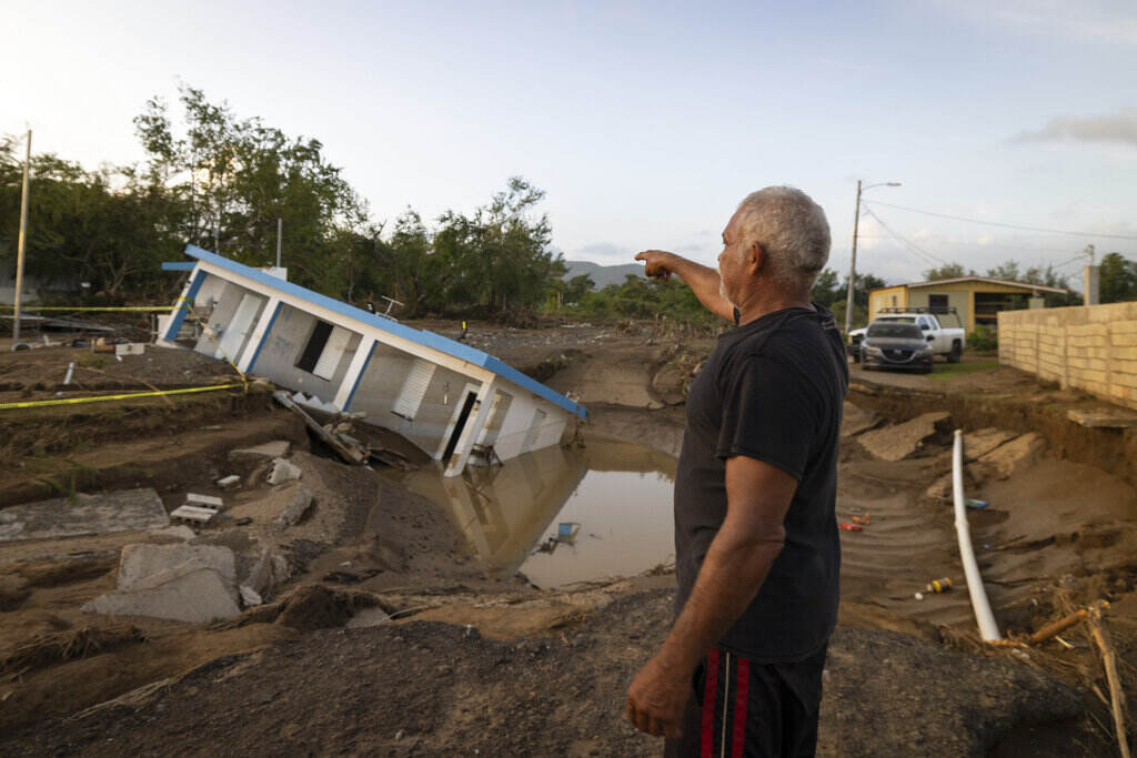 Puerto Rico Tropical Weather A man gestures towards a building sunk into mud.