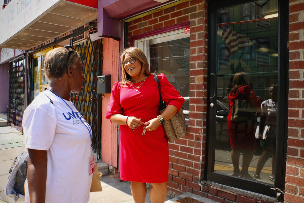 quetcylozada-district7-03 A woman in a red dress talks to another person outside of a brick building.