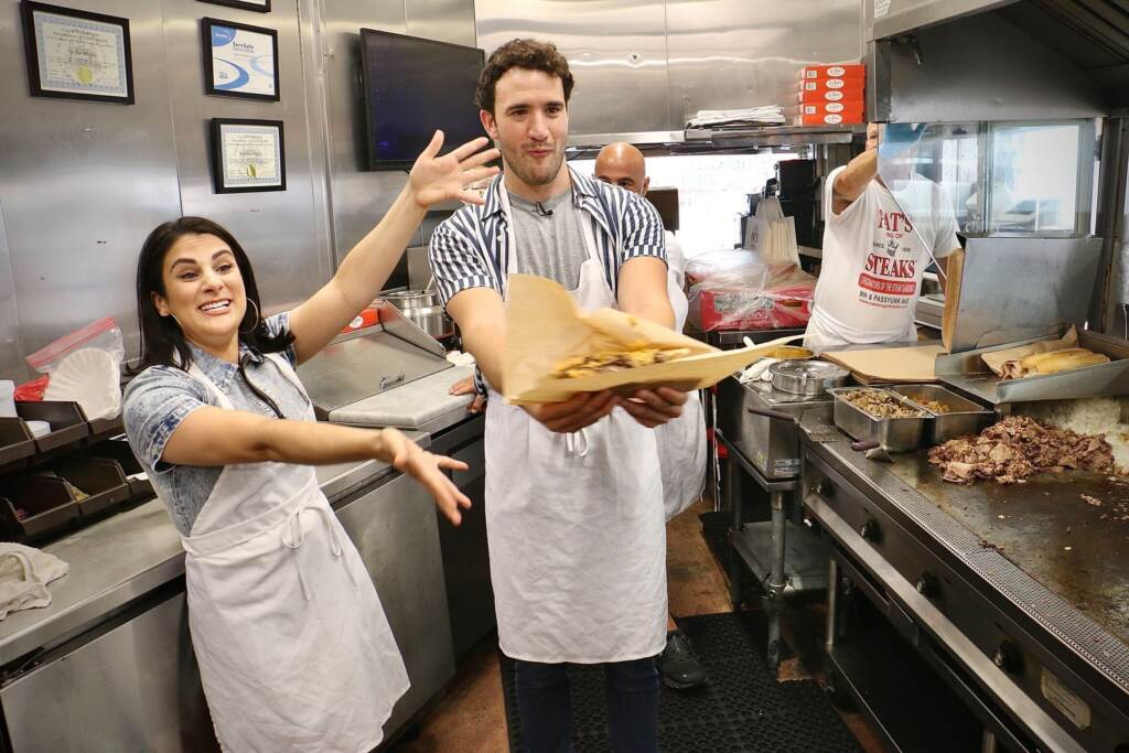 rocky-pats-steaks-e-lee-2022-09-07-3 Gianna Yanelli (left), who portrays Adrian in Walnut Street Theatre’s production of ‘’Rocky, the Musical,’’ and Matthew Amira, who portrays Rocky, make cheesesteaks at Pat’s King of Steaks in South Philadelphia. (Emma Lee/WHYY)